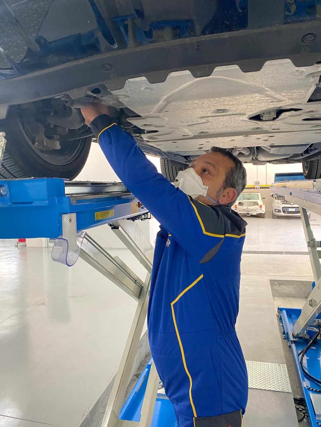 Tecnico al lavoro sotto una vettura sul ponte sollevatore